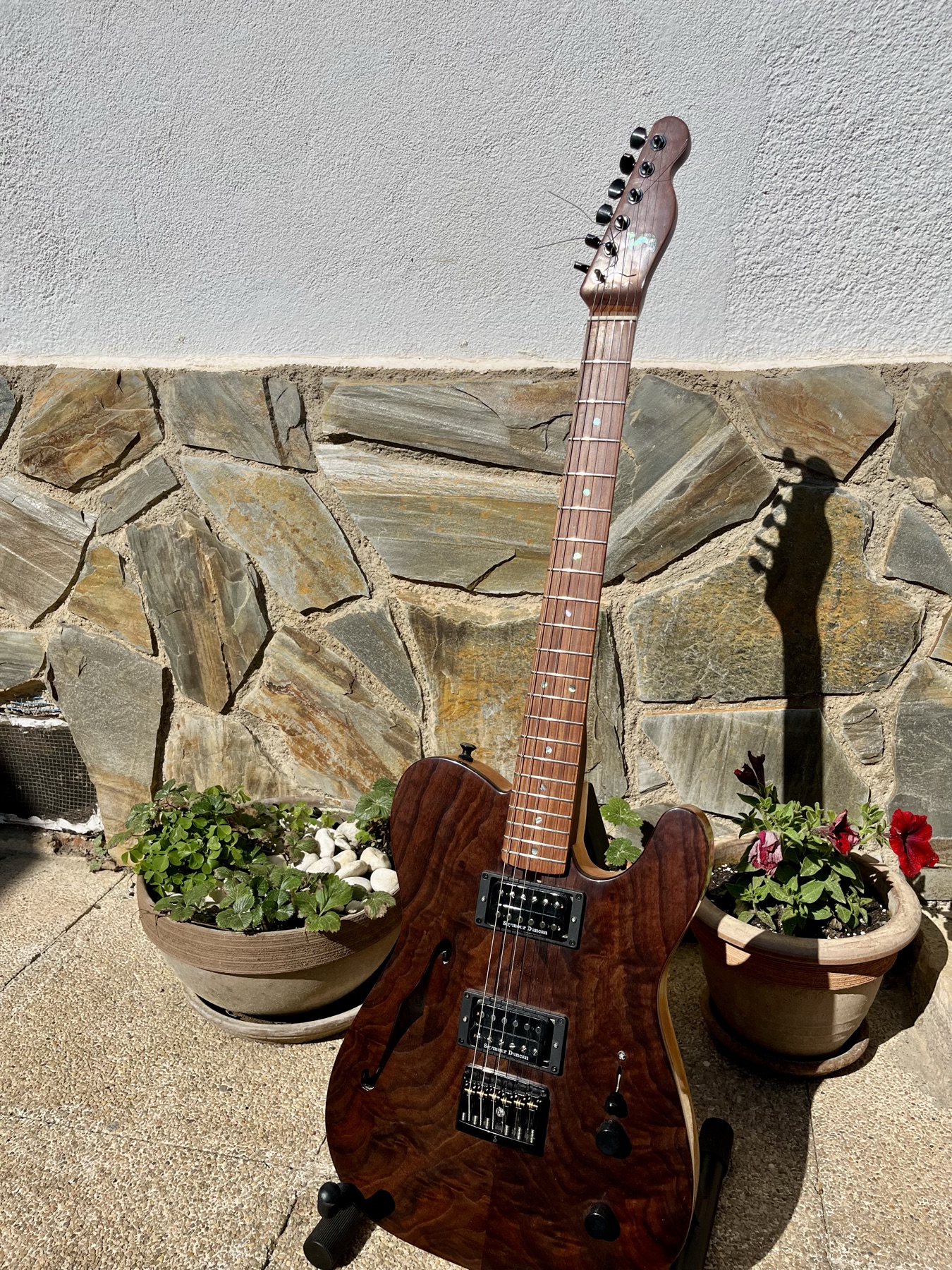 Completed walnut semi-hollow Telecaster leaning against a stone wall